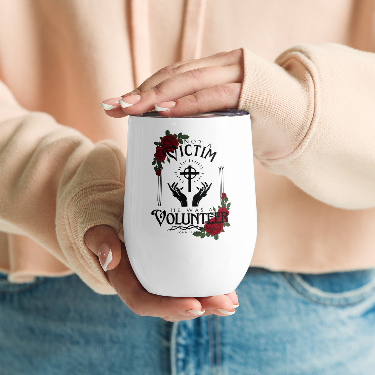 Person holding a white Not a Victim Christian wine tumbler while wearing a beige sweater